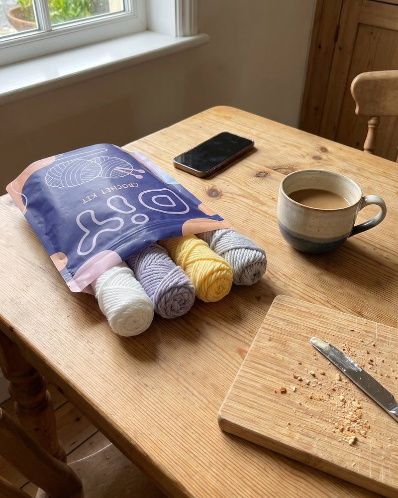 Den öppnade DIY-påsen med fyra garnnystan på ett köksbord bredvid en kaffekopp